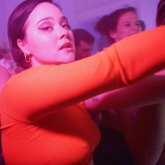 Gry Colding står på billedet med en langærmet rød t-shirt på og ser ind i kameraet