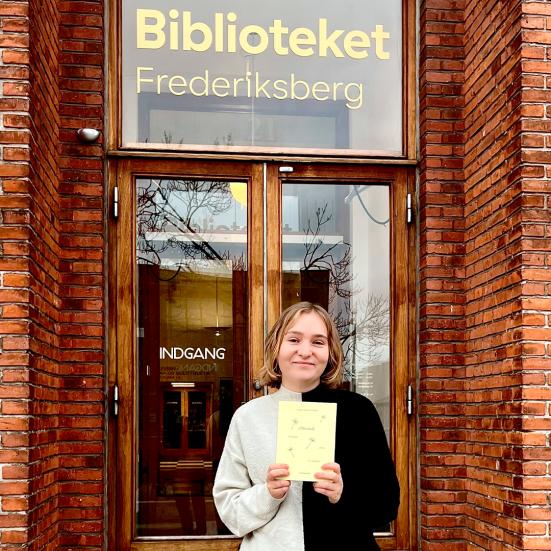 Litteraturformidler Amalie Pind med bogen Almanak foran bibliotekets indgang.