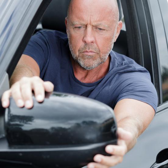 Mand der sidder i en bil og kigger i sidespejlet