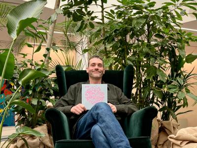 En sidende mand foran nogle planter viser bogen "Inger"