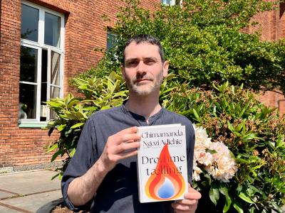 En mand står foran en bygning med bogen Drømmetælling i hænderne.