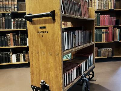 Historisk bogvogn i træ på en baggrund af fyldte bogreoler.