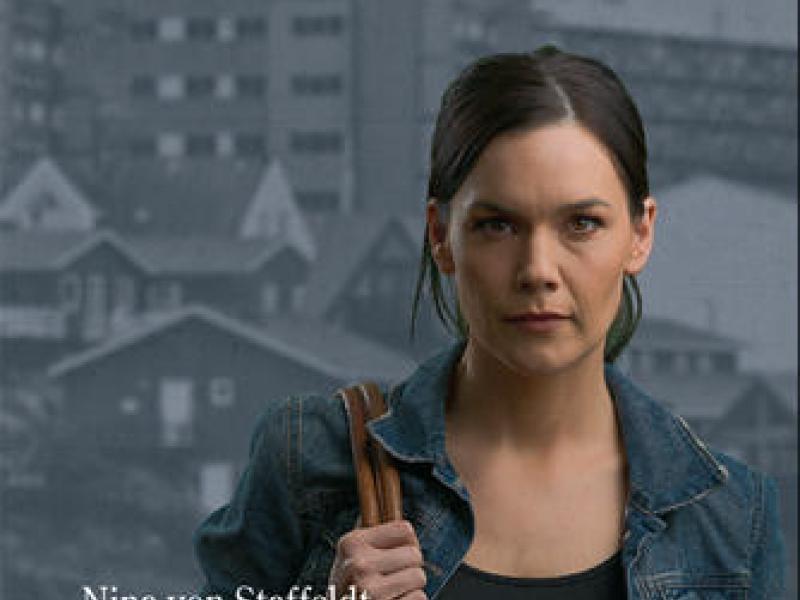 Cover til bogen 'Frosne beviser' af Nina von Staffeldt med kvinde foran et bybillede fra Nuuk.