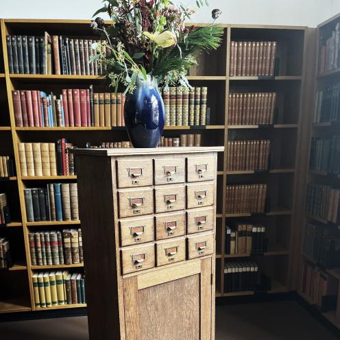 Billedet viser et kartotek. På møblet står der en vase med en buket blomster i 