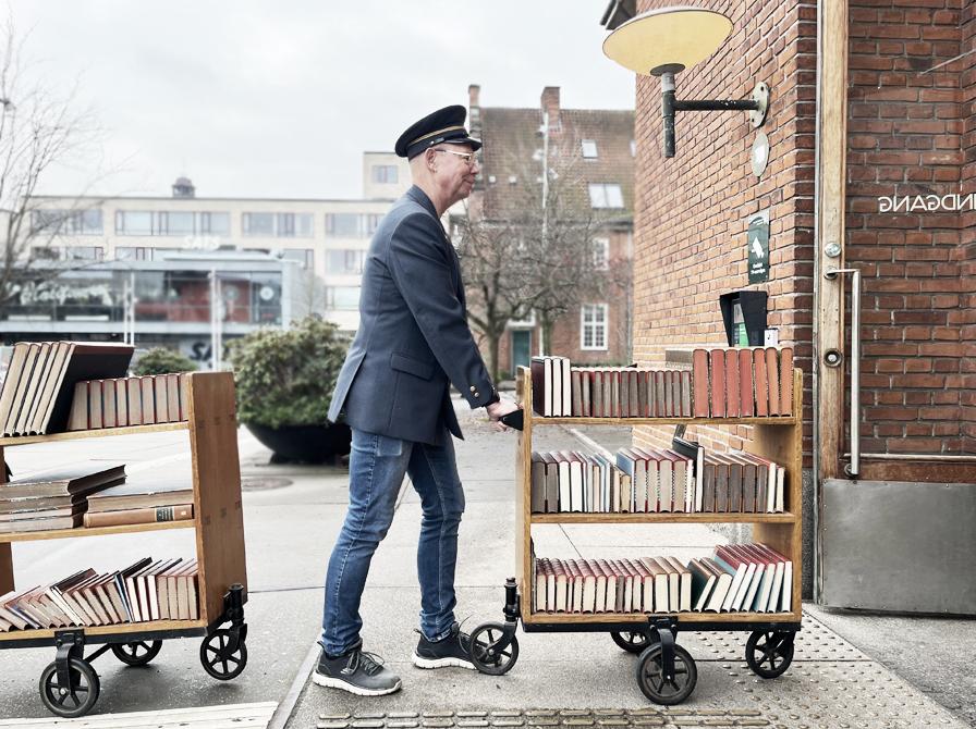 Bibliotekets nuværende betjent iført historisk jakke og kasket kørende med gammel bogvogn.