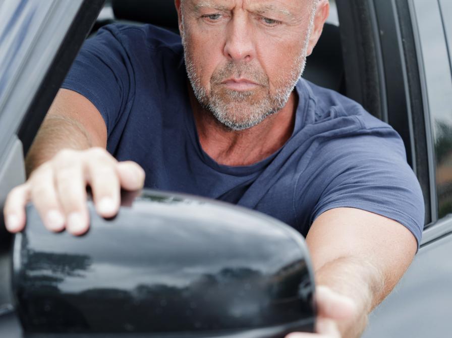 Mand der sidder i en bil og kigger i sidespejlet