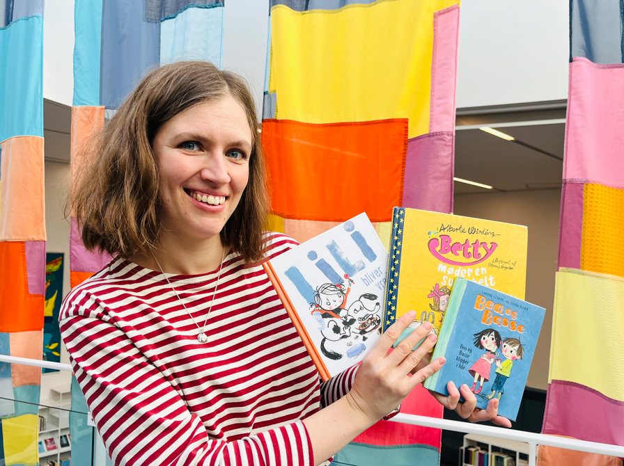 Bibliotekar holder de anbefalede bøger foran et farverigt bagtæppe