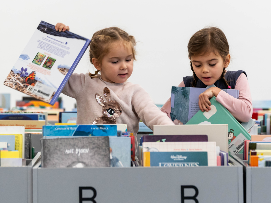 To piger på 3-5 år kigger på bøger i bogkasser