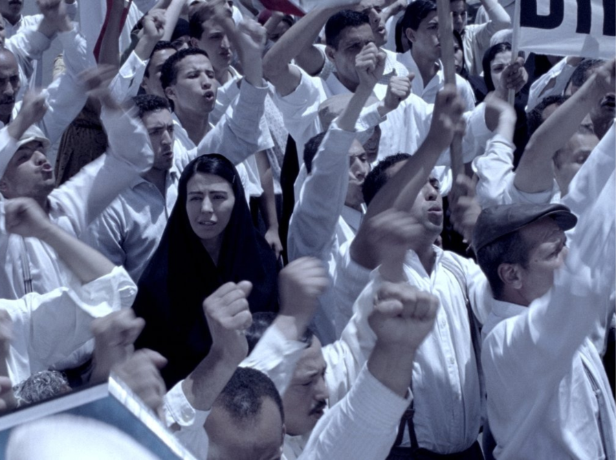 Kvinde med tørklæde i sort til demonstration med en masse mænd i hvidt